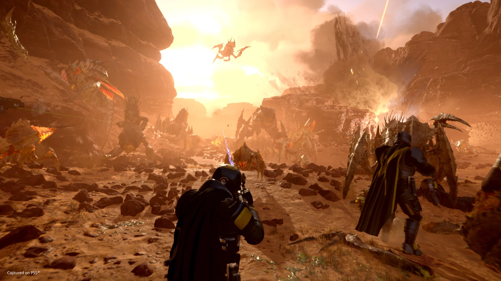 Helldivers stand in a rocky landscape beneath a huge insect-like creature, with bright sunlight behind the battlefield.