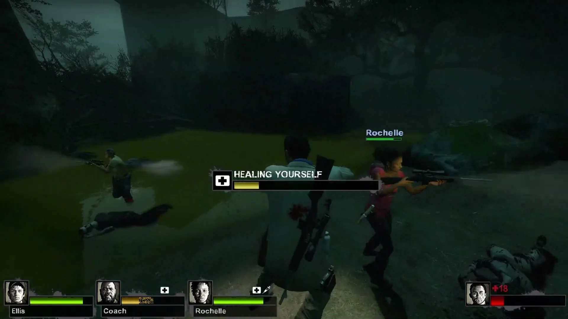 A survivor’s healing bar fills while Rochelle fires beside them on the wooded path in Left 4 Dead 2.